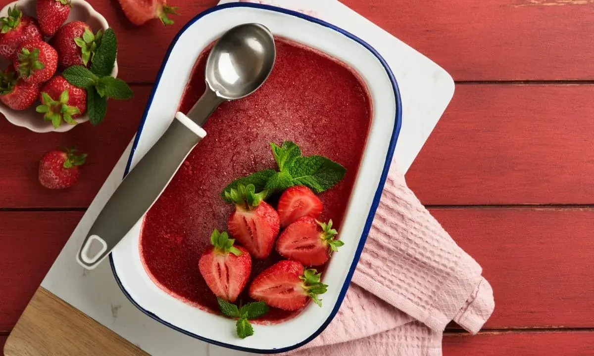 Orzeźwiający lody truskawkowe sorbet w naczyniu, ozdobione świeżymi truskawkami i miętą. Idealny na upalne dni.