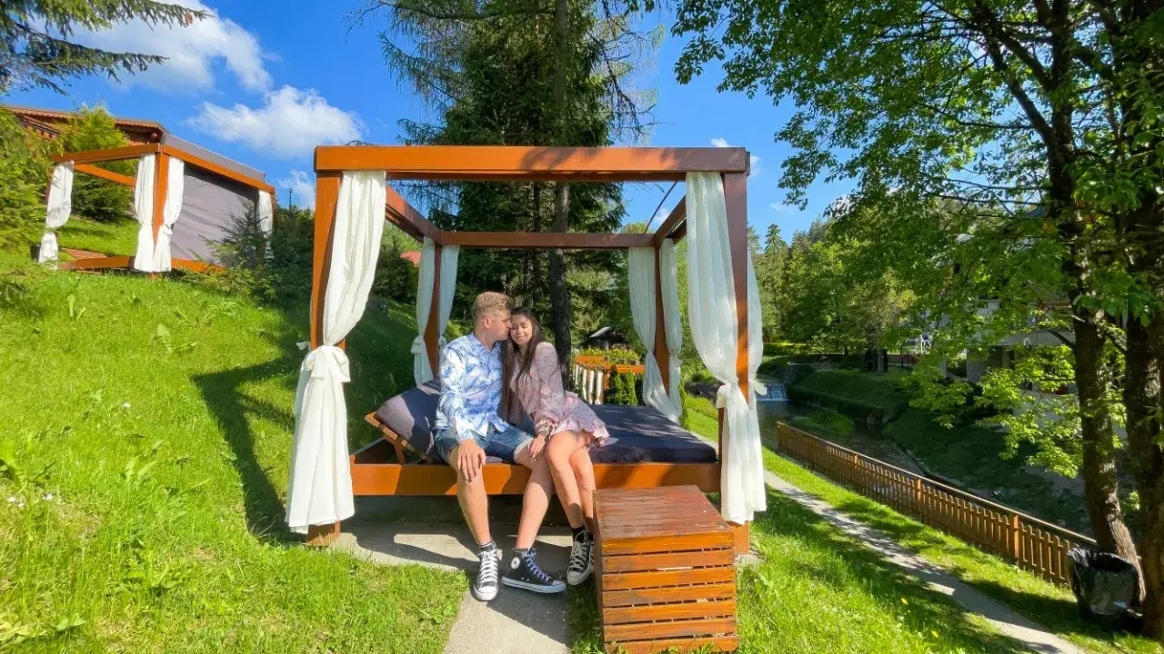 Idealne miejsce, gdzie na weekend we dwoje. Para odpoczywa na łóżku pod baldachimem w otoczeniu zieleni.