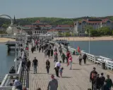 Tłum ludzi spaceruje po molo w Sopocie, jednym z nietypowych atrakcji Gdańska. W tle widać plażę i zabytkowe budynki.
