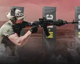 Mężczyzna w słuchawkach ochronnych i czapce z kamuflażem oddaje strzał na strzelnicy. W tle widoczne banery z logo M-TAC.