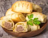 Stos pieczonego ciasta francuskiego z kiełbaską w środku, ozdobione natką pietruszki.