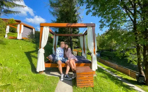 Idealne miejsce, gdzie na weekend we dwoje. Para odpoczywa na łóżku pod baldachimem w otoczeniu zieleni.
