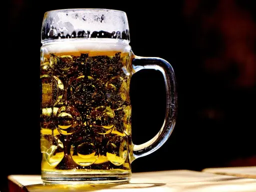 Szklany kufel z piwem, z charakterystycznymi wgłębieniami, to jeden z wielu rodzajów kufli do piwa. Piana i bąbelki dodają mu uroku.