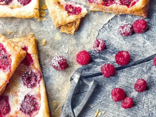 Pyszne ciasto francuskie z malinami, posypane cukrem pudrem. Idealne na letnie popołudnie.
