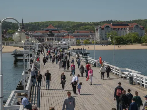 Tłum ludzi spaceruje po molo w Sopocie, jednym z nietypowych atrakcji Gdańska. W tle widać plażę i zabytkowe budynki.