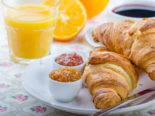 Idealne śniadanie francuskie: chrupiące rogaliki, dżemy, świeży sok pomarańczowy i kawa.