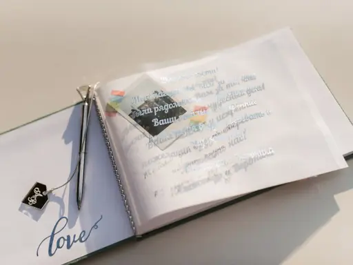 Otwarta księga gości z ozdobnym długopisem i napisem "love". Na otwartej stronie widnieją mądre życzenia ślubne od rodziców, ozdobione małym zdjęciem.