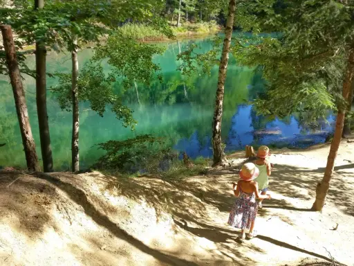 Dwie dziewczynki w słomkowych kapeluszach idą ścieżką nad turkusowe jezioro. Idealne miejsce, gdzie w góry z dziećmi latem.