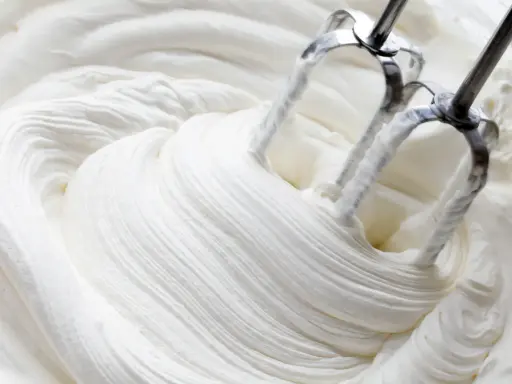 Mieszadła miksera ubijają puszystą, białą masę. Powstaje idealna bita śmietana, gotowa do dekoracji deserów.