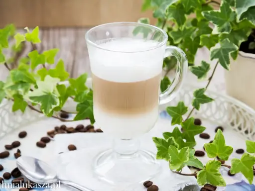 Jak zrobić latte? Warstwowy napój kawowy w szklance, otoczony bluszczem i ziarnami kawy.