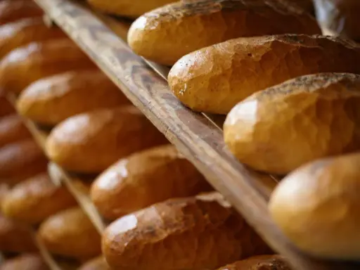 Rzędy czerstwego chleba na drewnianych półkach. Niektóre bochenki posypane są makiem.