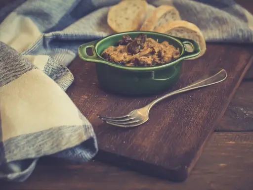 Pyszny bigos z szybkowaru w zielonej miseczce, obok kromki chleba i widelca.