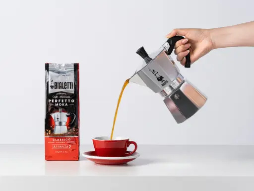 Popularna kawa Bialetti Moka wylewa się z kawiarki do czerwonej filiżanki.