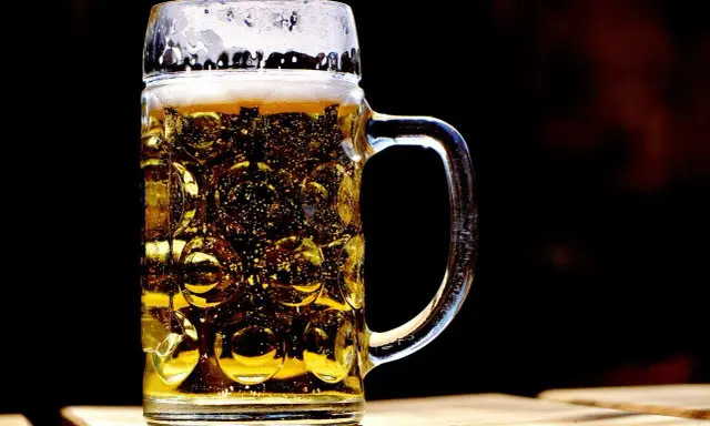 Szklany kufel z piwem, z charakterystycznymi wgłębieniami, to jeden z wielu rodzajów kufli do piwa. Piana i bąbelki dodają mu uroku.