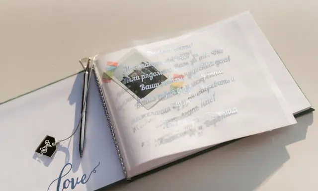 Otwarta księga gości z ozdobnym długopisem i napisem "love". Na otwartej stronie widnieją mądre życzenia ślubne od rodziców, ozdobione małym zdjęciem.