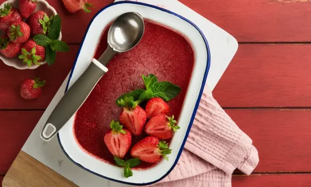 Orzeźwiający lody truskawkowe sorbet w naczyniu, ozdobione świeżymi truskawkami i miętą. Idealny na upalne dni.