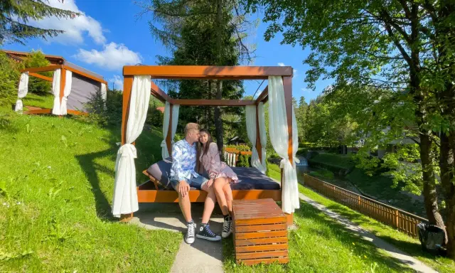 Idealne miejsce, gdzie na weekend we dwoje. Para odpoczywa na łóżku pod baldachimem w otoczeniu zieleni.