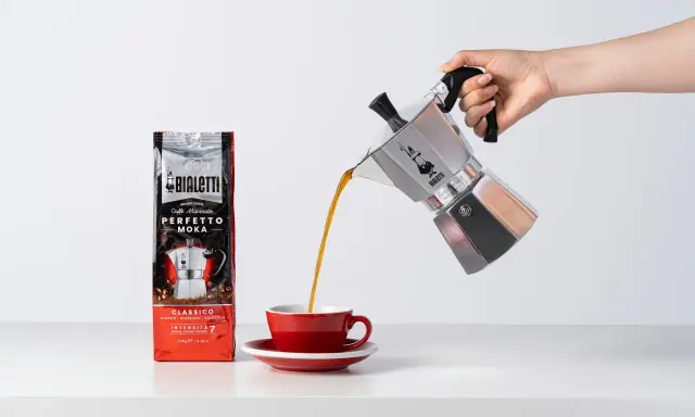 Popularna kawa Bialetti Moka wylewa się z kawiarki do czerwonej filiżanki.