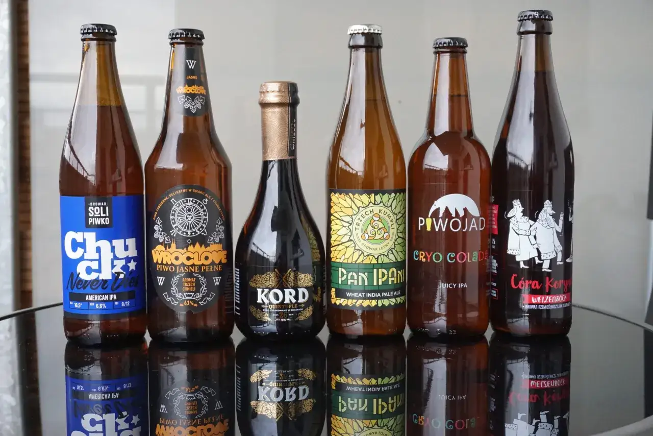 Siedem butelek piwa rzemieślniczego: American IPA, Piwo Jasne Pełne, Kord Quintuple, Pan Ipan Wheat India Pale Ale, Cryo Colada Juicy IPA, Córa Koryn Weizenbock.