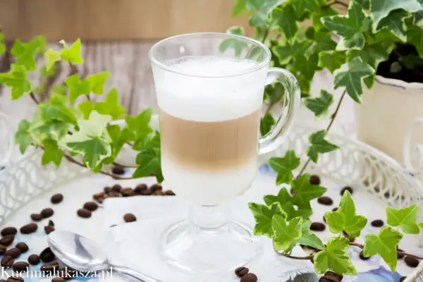 Jak zrobić latte? Warstwowy napój kawowy w szklance, otoczony bluszczem i ziarnami kawy.