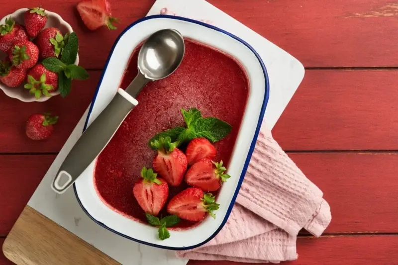 Orzeźwiający lody truskawkowe sorbet w naczyniu, ozdobione świeżymi truskawkami i miętą. Idealny na upalne dni.